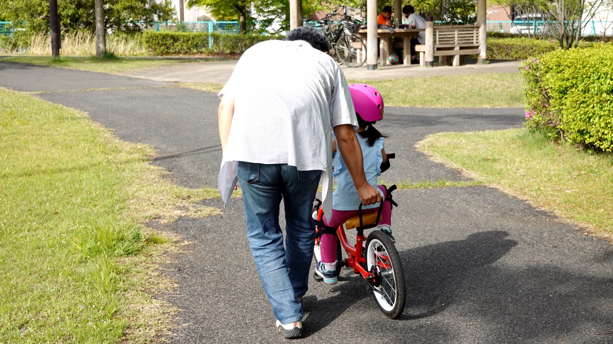 ケッターサイクルにペダルを付けて自転車の練習をする４歳の女の子とお父さん