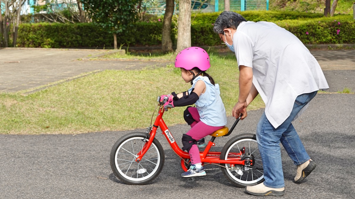 ケッターサイクルで自転車の練習をする女の子とサポートするお父さん